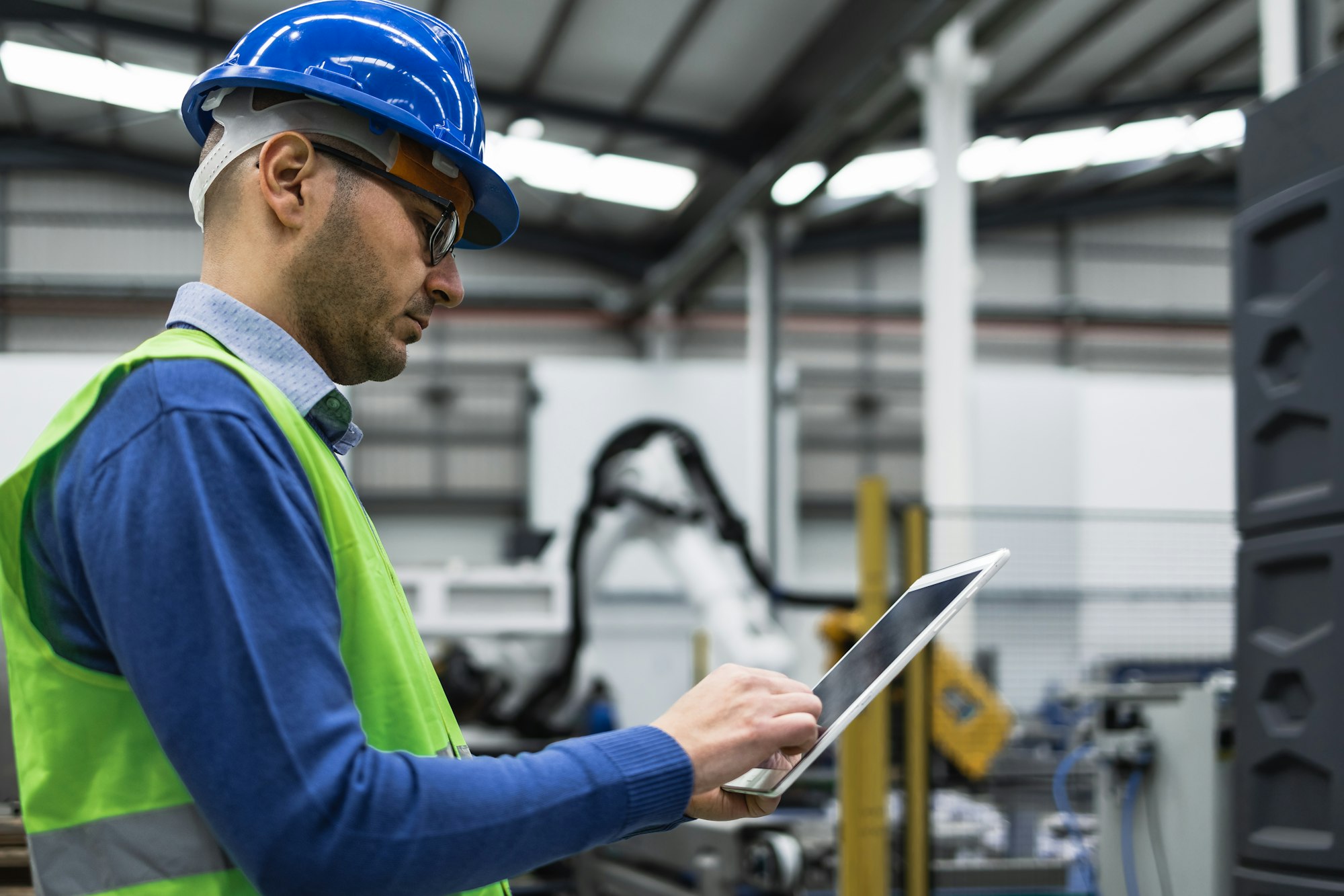 Engineer man working in robotic factory while monitoring the project on smart tablet